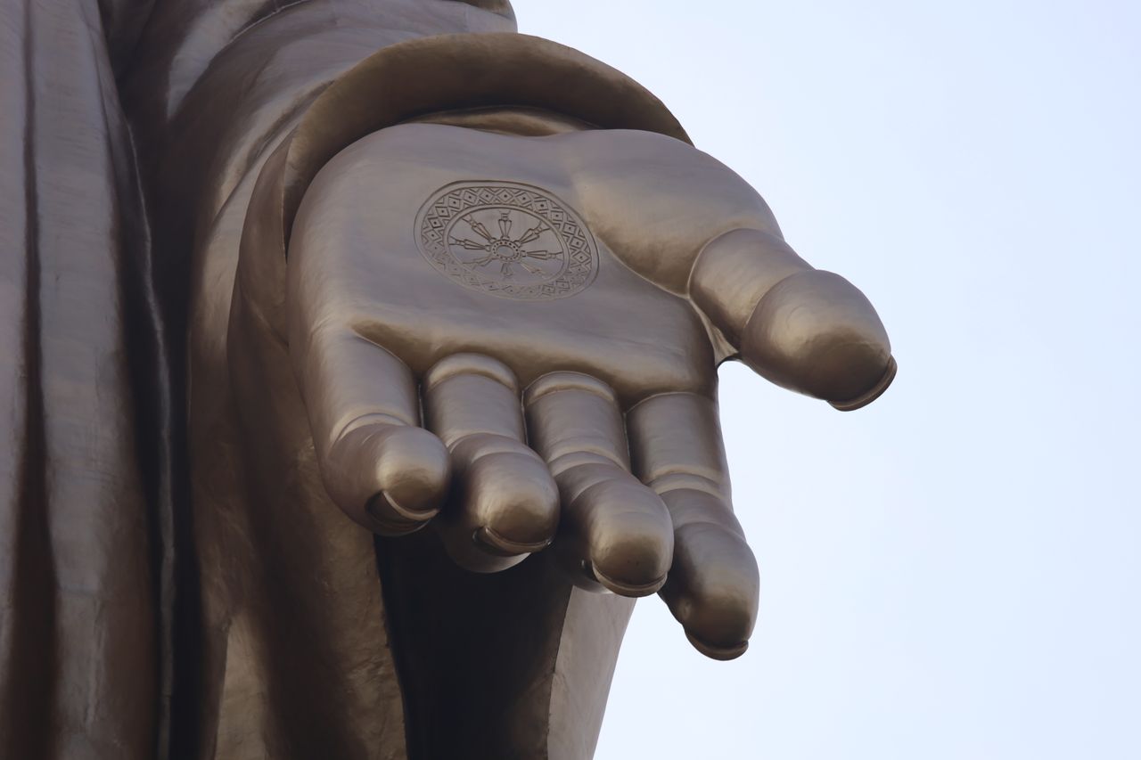 Detailed view of a Buddhist statue's hand with traditional religious symbol.